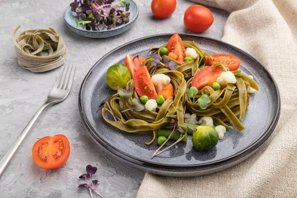 Tagliatelle yeşil ıspanaklı domates, bezelye ve mikroyeşil lahanalı gri beton arka plan ve keten tekstil. Yan görünüm, kapat.