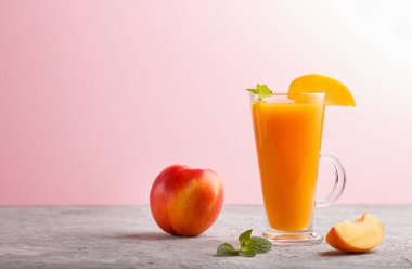 Gri ve pembe arka planda bir bardak şeftali suyu. Morninig, bahar, sağlıklı içki konsepti. Yan görünüm, boşluk kopyala.