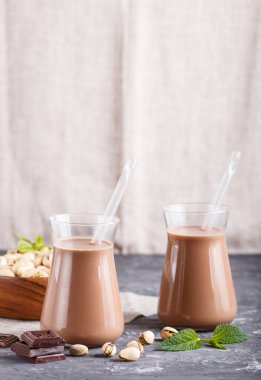 Süt ürünü olmayan organik pistache çikolatalı süt ve gri beton arka planda şam fıstıklı ahşap tabak. Vegan sağlıklı gıda konsepti, yakın çekim, yan görüş, kopyalama alanı.