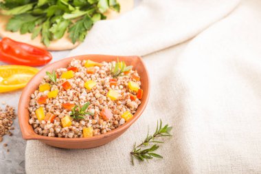 Kil kasede sebzeli karabuğday lapası gri beton arka plan ve keten tekstil. Yan görüş, seçici odaklanma, kopyalama alanı. Rus geleneksel mutfağı.