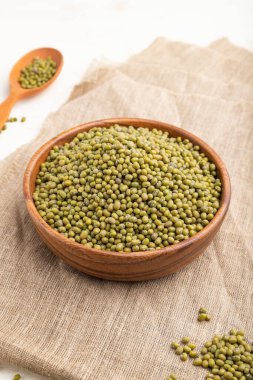 Tahta kase, çiğ yeşil fasulye çekirdeği ve beyaz arka planda ahşap kaşık ve keten tekstil. Yan görünüm, kapat.