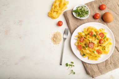 Beyaz ahşap arka planda domates, yumurta, susam ve mikroyeşil lahanalı Reginelle irmik makarna ve keten tekstil. Üst görünüm, düz görünüm, kopyalama alanı.