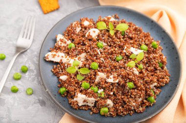 Yeşil bezelyeli kinoa lapası ve gri beton arka planda seramik tabakta tavuk ve turuncu tekstil. Üst görünüm, kapat, seçici odaklanma.