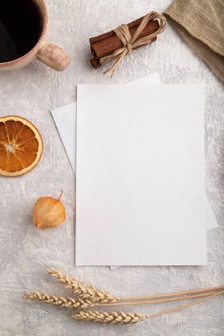Beyaz kağıt davetiye kartı, buğday, çörek, bir fincan kahve, keten tekstil, gri beton arka planda fizsalis. Boşluk, düzlük, üst görünüm, durgun yaşam, kopyalama alanı.