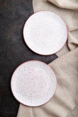 Siyah beton arka plan ve keten tekstil üzerine iki boş beyaz plaka. Üst manzara, kapat, düz yat..