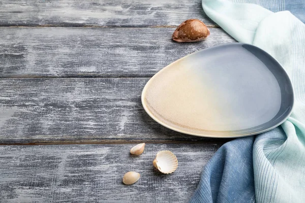 Gri ahşap arka planda boş mavi seramik tabak ve mavi tekstil. Yan görünüm, boşluk kopyala.
