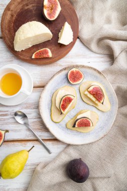 Beyaz ahşap arka planda armut, süzme peynir, incir ve bal ile yaz iştahı ve keten tekstil. Üst manzara, düz yatak, yakın çekim..