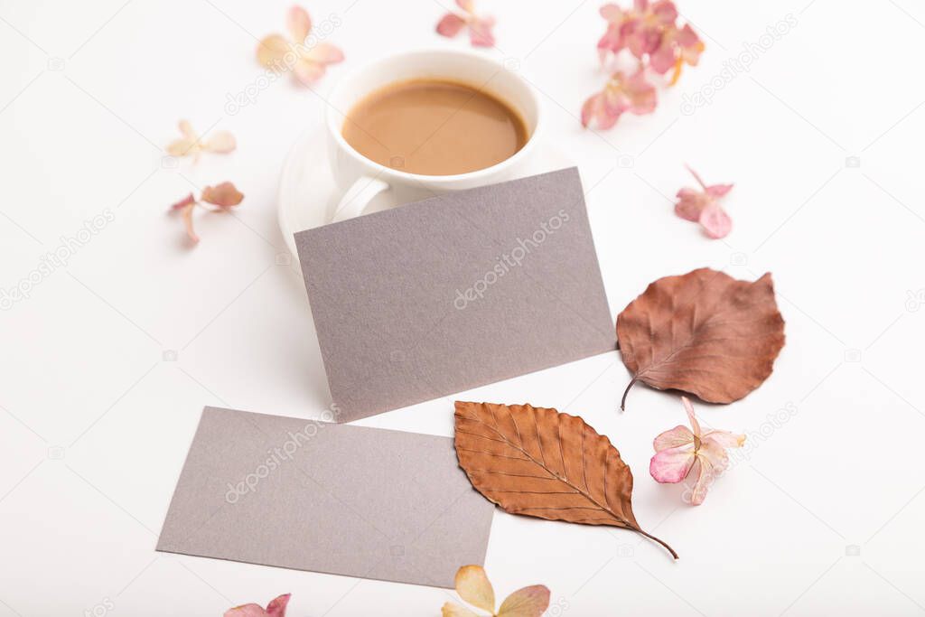 Composition with gray paper business card, brown beech autumn leaves, hydrangea flowers and cup of coffee. mockup on white background. Blank, side view, still life, copy space.