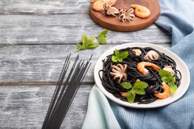 Karides, karides ve gri ahşap zemin ve mavi tekstil üzerine küçük ahtapotlu siyah mürekkep balığı makarnası. Yan görünüm, boşluk kopyala.