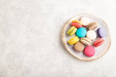 Gri beton arka planda seramik tabakta çok renkli badem kurabiyeleri. Üst görünüm, kopyalama alanı, durgun hayat. Kahvaltı, sabah, konsept..