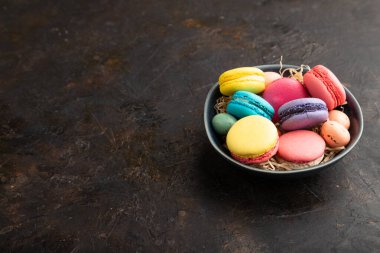 Çok renkli badem kurabiyeleri ve siyah beton arka planda seramik kasede çikolatalı yumurtalar. Yan görüş, kopyalama alanı, durağan hayat. Kahvaltı, sabah, konsept..