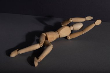 Ahşap manken gri arka planda koruma pozisyonunda yatıyor. Yalnızlık, şiddet, hassasiyet, depresyon bozukluğu konsepti. Boşluğu kopyala, sert ışık.