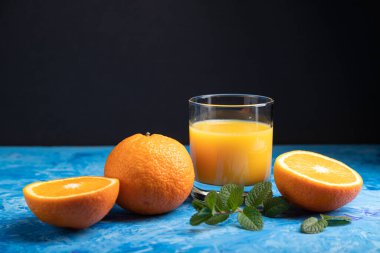 Siyah ve mavi arka planda naneli bir bardak portakal suyu. Sert ışık, kontrast. Yan görünüm, boşluk kopyala.