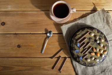 Ev yapımı çikolatalı kek, karamel kremalı ve bademli tahta arka planda bir fincan kahve ve keten tekstil. Üst görünüm, sabit ışık, kopyalama alanı, düz uzanma.