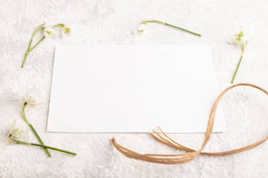 Gri beton arka planda bahar kardelen galanthus çiçekli beyaz kağıt maketi. Boş, kartvizit, yan görüş, fotokopi alanı, natürmort hayat. bahar konsepti.