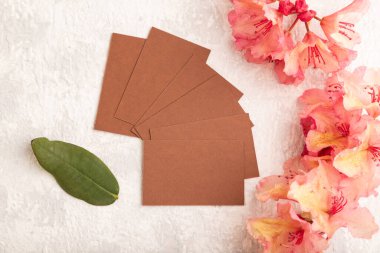 Gri çimento arka planda pembe açelya çiçekleri olan kahverengi kartvizit. Üst görünüm, düz görünüm, kopyalama alanı, model, şablon, bahar, yaz minimalizmi kavramı.