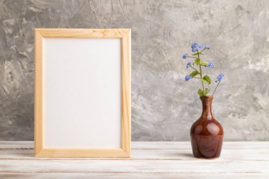 Ahşap çerçeve, gri beton arka planda seramik vazoda mavi unutma beni çiçekleri. Yan görünüm, kopyalama alanı, natürmort, model, şablon, bahar, yaz minimalizmi kavramı.
