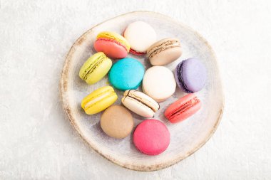 Gri beton arka planda seramik tabakta çok renkli badem kurabiyeleri. Üst manzara, yakın çekim, durgun hayat. Kahvaltı, sabah, konsept..