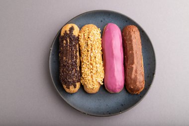 Ekler, geleneksel Fransız tatlıları gri pastel arka planda mavi seramik tabakta. Üst manzara, düz yatak, yakın çekim, durgun hayat. Kahvaltı, sabah, konsept..