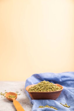 Çiğ yeşil fasulye kabı ve gri ve turuncu arka planda ahşap kaşık ve mavi tekstil. Üst görünüm, seçici odak, kopyalama alanı.