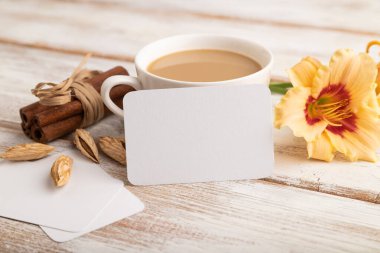 Beyaz kağıt kartvizit modeli, turuncu zambak çiçeği ve beyaz ahşap arka planda bir fincan kahve. Boş, yan görüş, kopyalama alanı, natürmort hayat. bahar konsepti.