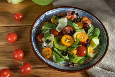 Pac choi lahana, kivi, domates, kumkatlı vejetaryen salatası, ahşap arka planda mikroyeşil lahanalar ve keten tekstil. Sert ışık, kontrast. Yan görünüm, kapat.