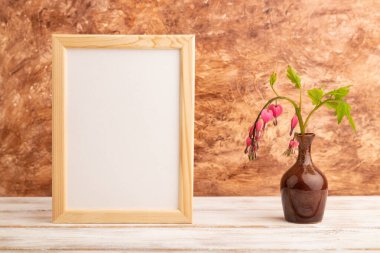 Ahşap çerçeve pembe dicentra, kırık kalp seramik vazoda kahverengi beton arka planda. Yan görünüm, kopyalama alanı, modelleme, şablon, bahar, yaz minimalizmi kavramı.