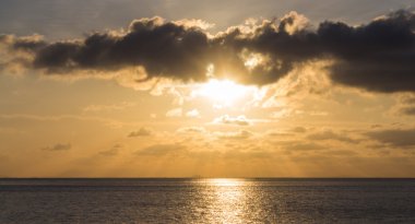 Bulutların arasından güneş ışınları ile denize günbatımı