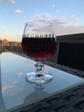 Cam bir masada, mavi gökyüzüne karşı bir bardak kırmızı şarap, kırmızı şaraplı kristal bardak.