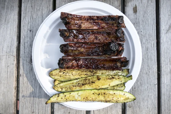 Costelas de porco grelhadas e lanças de abobrinha na placa de papel do churrasco ao ar livre — Fotografia de Stock