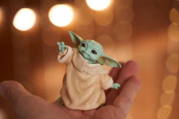 November, 2020: Display of Baby Yoda, an action figures, standing on hand. Christmas background bokeh effect. Macro effect photo. — Stock Photo, Image