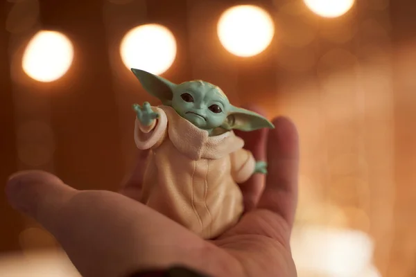 November, 2020: Display of Baby Yoda, an action figures, standing on hand. New Years bokeh effect. Macro effect photo. — Stock Photo, Image