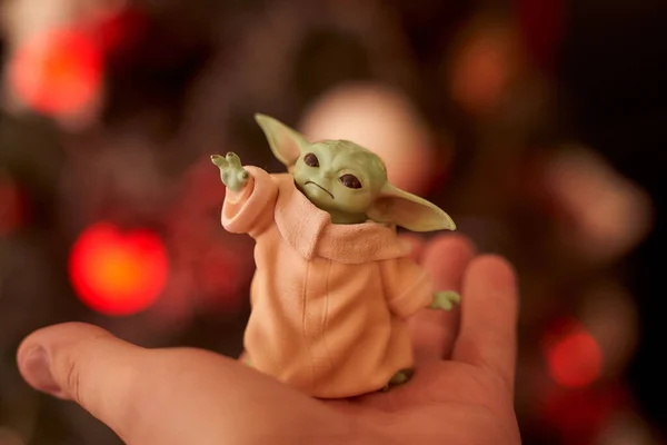 November, 2020: Display of Baby Yoda, an action figures, standing on hand. Christmas background bokeh effect. Macro effect photo. — Stock Photo, Image