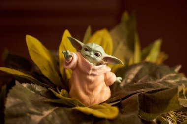 Kasım 2020: Yeşil yaprakların üzerinde duran oyuncak bebek Yoda 'nın görüntüsü
