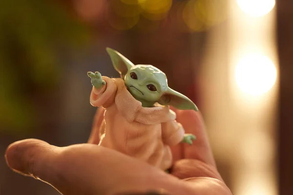 November, 2020: Display of Baby Yoda, an action figures, standing on hand. New Years bokeh effect. Macro effect photo. — Stock Photo, Image