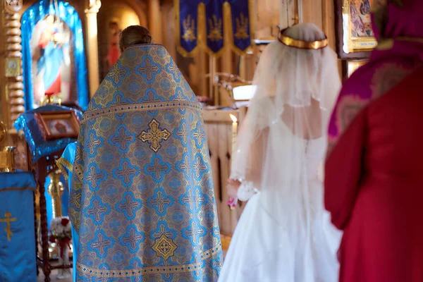 La espalda de un sacerdote en una hermosa sotana se levanta ante el altar. Una boda sagrada. Novia en el fondo — Foto de Stock