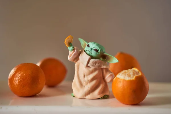 Dec, 2020: Display of Baby Yoda, an action figures, standing with orange tangerines Bokeh effect. — Stock Photo, Image