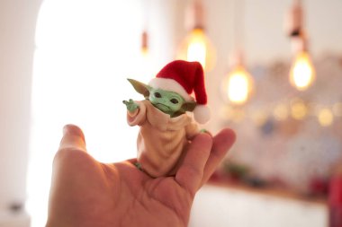 Aralık 2020: Bebek Yoda 'nın görüntüsü, bir aksiyon figürü, Noel arkaplanında kırmızı başlık takıyor. Bokeh etkisi. 
