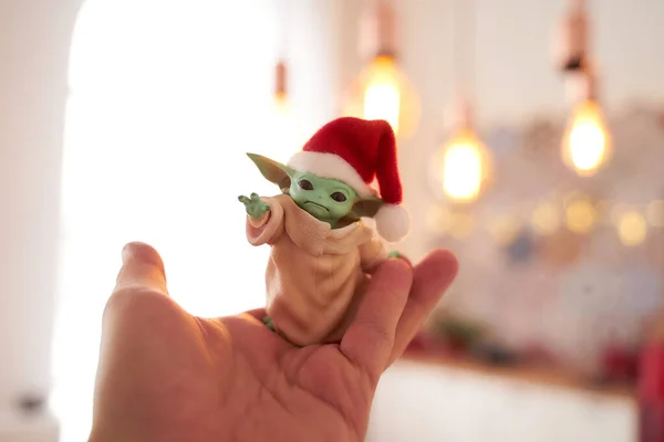 Aralık 2020: Bebek Yoda 'nın görüntüsü, bir aksiyon figürü, Noel arkaplanında kırmızı başlık takıyor. Bokeh etkisi. 