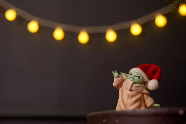 Aralık 2020: Bebek Yoda 'nın görüntüsü, bir aksiyon figürü, Noel arkaplanında kırmızı başlık takıyor. Bokeh etkisi. 