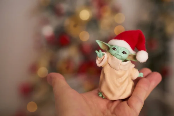 Aralık 2020: Bebek Yoda 'nın görüntüsü, bir aksiyon figürü, Noel arkaplanında kırmızı başlık takıyor. Bokeh etkisi. 