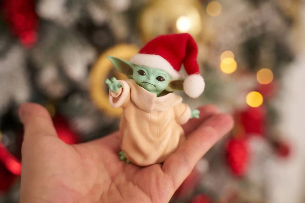 Aralık 2020: Bebek Yoda 'nın görüntüsü, bir aksiyon figürü, Noel arkaplanında kırmızı başlık takıyor. Bokeh etkisi. 