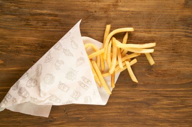 Kağıt üzerinde patates kızartması ahşap bir arka planda yatıyor. Soslar ve yeşiller. Yüksek kalite fotoğraf