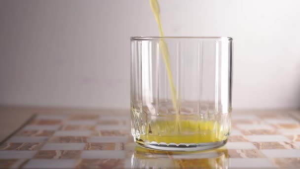 Een prachtig glas waarin sinaasappelsap wordt gegoten. Lichte achtergrond — Stockvideo