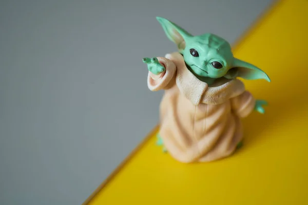 Marzec, 2021: Wyświetlacz Baby Yoda, figurki akcji, stoi na szaro-żółtym tle — Zdjęcie stockowe