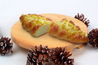 Taze pişirilmiş tatlı peynir ekmeği, ahşap panoda iki dilim çam kozalağı süslemesi