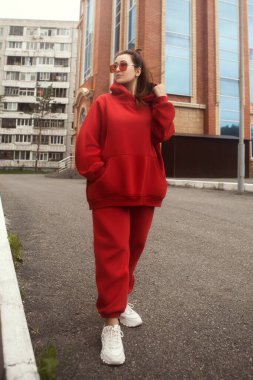 Genç bir kadın kırmızı, sıcacık bir spor kostümü içinde poz veriyor.