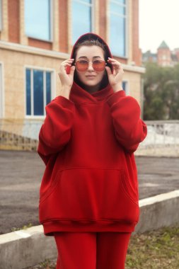 Genç bir kadın kırmızı, sıcacık bir spor kostümü içinde poz veriyor.