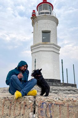 Bir adam ve bir köpek deniz fenerinin yanında oynuyorlar.