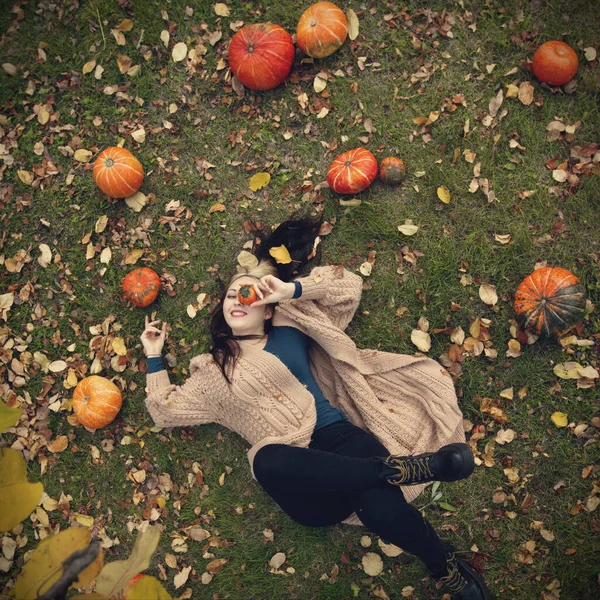 Güzel bir kadın çimlerin üzerinde yatıyor. Üst Manzara. Balkabaklarının yanında yatıyor. Gözünün yanında dekoratif bir balkabağı tutuyor..